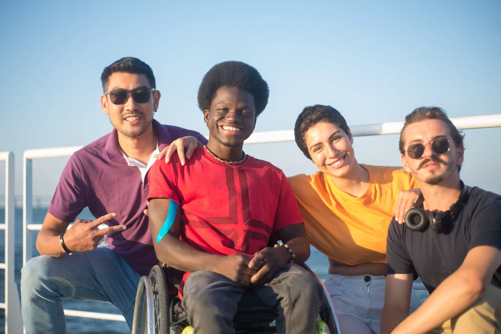 A group of friends smiling together outdoors, including a wheelchair user