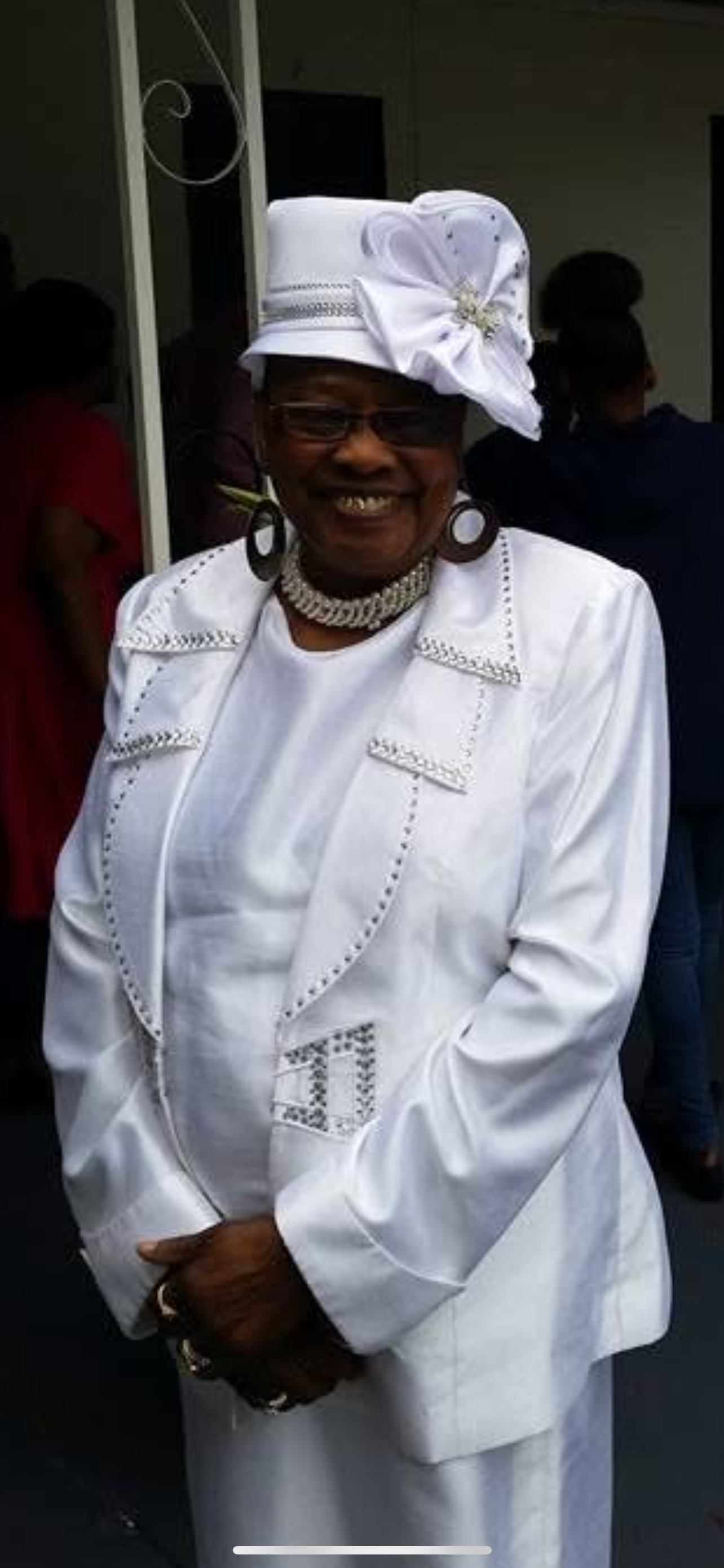A smiling woman dressed in an elegant white suit and hat